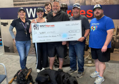 Five people and two relaxed service dogs in vests pose with an oversized ceremonial check for $752,800 made out to WNYHeroes for the Pawsitive for Heroes program.