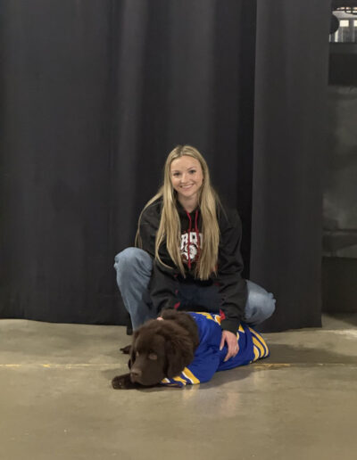 Mac the dog laying on the ground. A young blond haired women kneeling behind Mac